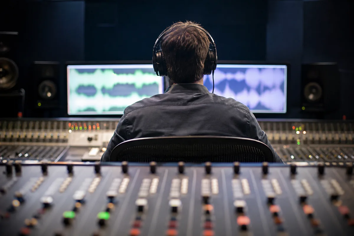 Technicien son de dos devant une console de mixage en studio de postproduction