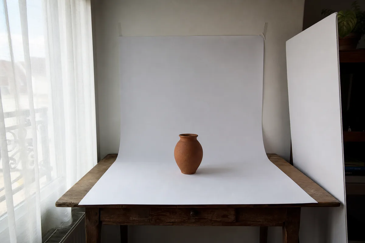 Table de prise de vue installée près d’une fenêtre, poterie posée sur un fond de papier blanc en courbe