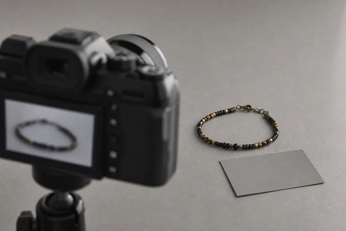 Appareil photo sur trépied de table cadrant un bijou artisanal posé sur un fond gris neutre